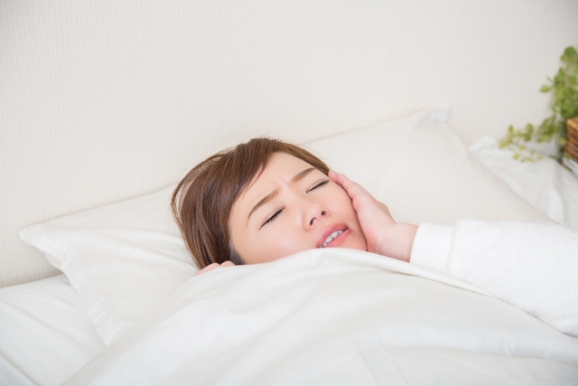 就寝時に頬をおさえる女性
